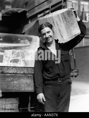 1930 ICE DELIVERY MAN CARRYING LARGE BLOC DE GLACE SUR L'ÉPAULE LOOKING AT CAMERA Banque D'Images