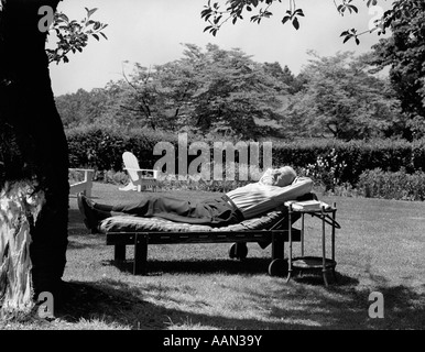 Années 1950, un homme âgé dans jardin allongé sur une chaise longue en vertu de l'arbre Banque D'Images
