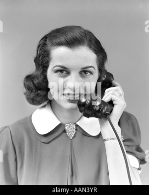 Années 1930 Années 1940 BRUNETTE WOMAN SMILING HOLDING TÉLÉPHONE À L'OREILLE ROBE AVEC COL BLANC LOOKING AT CAMERA Banque D'Images