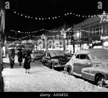 Années 1940 Années 1950 SCÈNE DE RUE DE LA VILLE D'HIVER AVEC LES PIÉTONS DANS LA NEIGE LES LUMIÈRES DE NOËL Banque D'Images