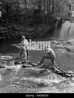 1950 COUPLE QUI PREND LA PHOTO D'UNE FEMME DE MOUCHE AU RUISSEAU AVEC CASCADE Banque D'Images