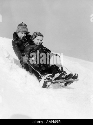 1930 SMILING BOY AND GIRL SLEDDING DOWNHILL Banque D'Images