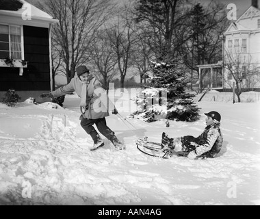 1950 FEMME MÈRE TIRANT BOY fils sur un traîneau en hiver Banque D'Images