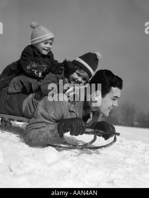 1930 Père et fille fils empilés sur les pentes de traîneau DANS LA NEIGE EN RIANT Banque D'Images