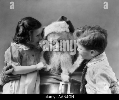 1930 PETIT GARÇON AVEC GIRL WHISPERING PÈRE NOËL DIT CE QU'ELLE VEUT POUR NOËL Banque D'Images