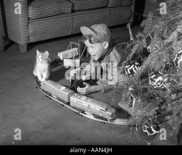 1950 garçon EN COSTUME INGÉNIEUR DE TRAIN ÉLECTRIQUE AVEC LECTURE DÉFINIE PAR L'ARBRE DE NOËL ET CHATON PISCINE Banque D'Images