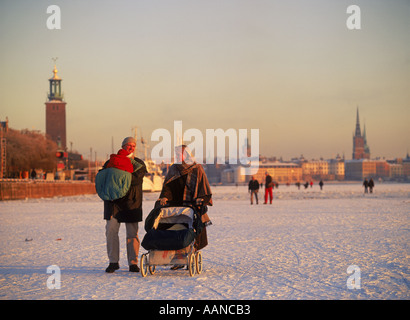 L'ensemble chariot bébé poussant la famille Riddarfjarden gelés en hiver avec l'Hôtel de Ville de Stockholm ou Stadshuset sur la gauche Banque D'Images