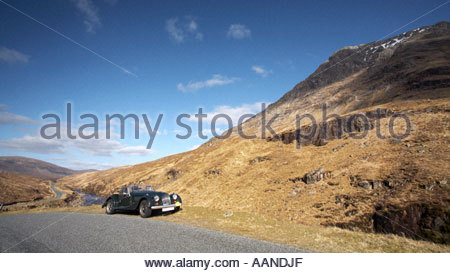 Un classic racing green Morgan sportscar, garé dans un glen écossais sur une journée ensoleillée avec des pics enneigés Banque D'Images