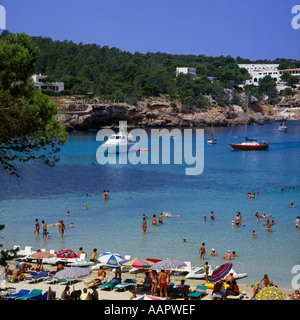 Vue sur plage vacances soleil transats décideurs brollies bateaux mer bleue et la baie de Portinatx, à Ibiza Baléares Espagne sur Banque D'Images