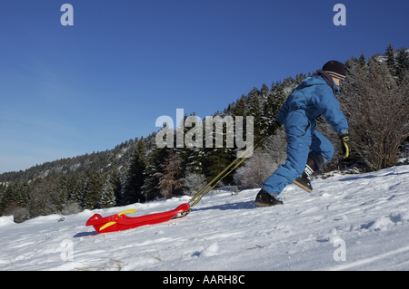 Remorquage d'un garçon en montée de traîneau dans la neige, Lans-en-Vercors, Isère, France. Banque D'Images