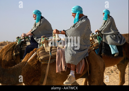 Close up de trois touristes britanniques dans les vêtements du désert à cheval sur le dos de chameaux dans le désert du sahara à Douz, Tunisie Banque D'Images