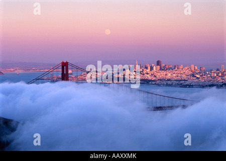 Horizon de San Francisco dans le brouillard flottant au-dessus du Golden Gate Bridge au coucher du soleil avec pleine lune en Californie Banque D'Images