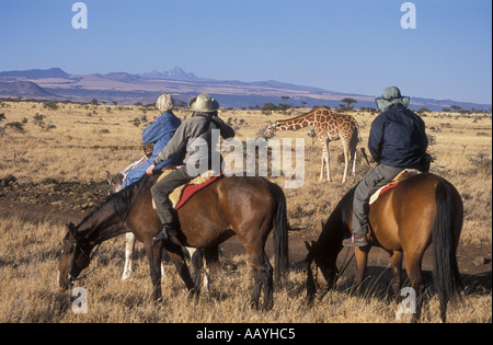 Trois cavaliers près de giraffe réticulée à Lewa Downs Kenya Afrique de l'est le mont Kenya peut être vu dans l'arrière-plan Banque D'Images