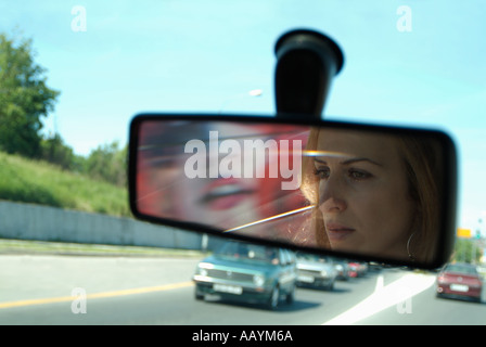 Femme dans le rétroviseur d'une voiture roulant sur une route très fréquentée Banque D'Images