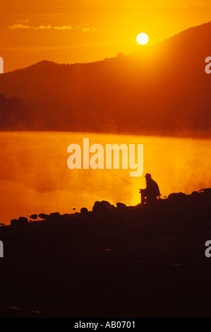 Homme est assis silhouetté par lever de soleil sur les montagnes qu'il pêche dans le lac estes CO Banque D'Images