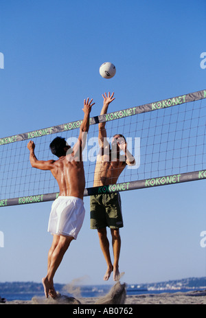 Deux hommes en maillot à l'un vers le haut leap spike et l'autre pour bloquer un terrain de volley-ball sur le net au cours d'un jeu sur la plage Banque D'Images