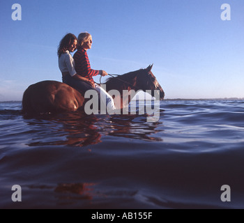 Couple riding a horse bareback dans le lac au coucher du soleil Banque D'Images