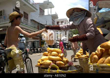 Garçon sur location l'achat des petits pains frais froim chapeau conique femme vendeur de rue Phan Thiet Vietnam du sud-est Banque D'Images