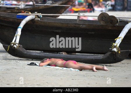 Pink bikini woman sunbathing on beach à côté de bateau outrigger open sud de Goa Palolem Inde Banque D'Images