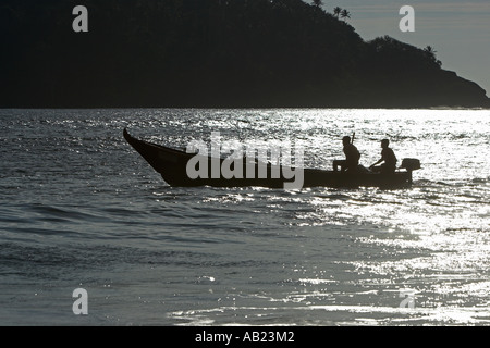 Deux hommes en bateau hors-bord ouvert outrigger silhouetté sur l'eau d'argent du Sud Inde Goa Palolem Banque D'Images