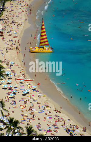 Regardant vers le bas sur la plage de Waikiki Hawaï un catamaran jaune a tiré vers le haut sur la plage remplie sunbather Banque D'Images