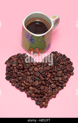 Tasse de café et grains de café dans un tas en forme de coeur sur fond rose Banque D'Images