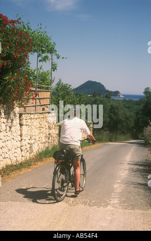 Femme cyclisme vers la plage de Keri et de Limni Keriou village avec Marathonisi Island à venir sur l'île grecque de Zakynthos Banque D'Images