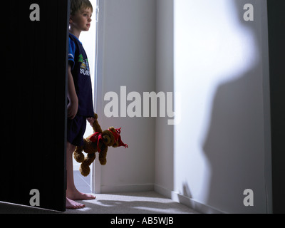 La marche de l'enfant dans la maison pendant la nuit qui sort de la lumière avec l'anticipation vêtus de pj et de transporter son ours en peluche préféré Banque D'Images