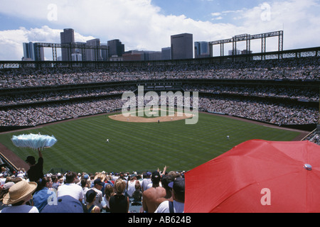 Denver Colorado USA foule remplit Coors Field pour l'après-midi d'un match de baseball couple cherche un abri contre le soleil chaud sous parapluie rouge Banque D'Images