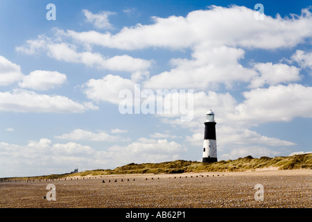 Rejeter Head Lighthouse à distance avec plage en premier plan dans un ciel ensoleillé nuageux jour lumineux Banque D'Images