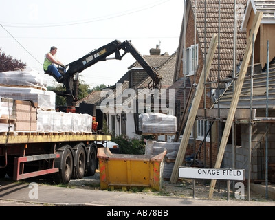 Grue de charge par déchargement mécanique de camion articulé avec chargement de tuiles de toit enveloppées sous film rétractable sur des palettes vers le chantier de construction Angleterre Royaume-Uni Banque D'Images