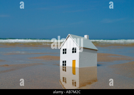 Maison modèle de sombrer dans le sable avec des vagues de l'océan en arrière-plan Banque D'Images