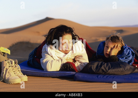 Jeune femme avec garçon dans le désert, se trouvant côte à côte sur leur ventre sur le tapis de camping, réveille, Maroc, dans le sud du Maroc. Banque D'Images