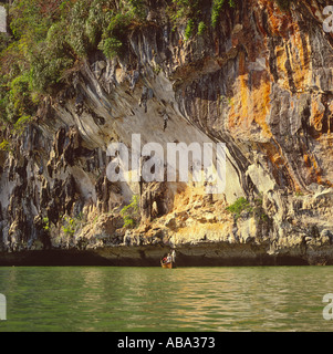 Les hommes en petit bateau de pêche à la base des falaises calcaires spectaculaires et de formations rocheuses à Phang Nga en Thaïlande Banque D'Images