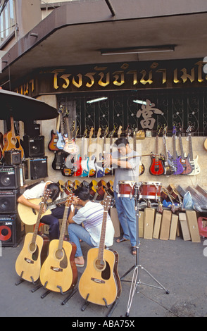 Guitares sur la vente et la manipulation des hommes jouant à l'extérieur de l'atelier à Khlong Road, Bangkok, Thaïlande Banque D'Images