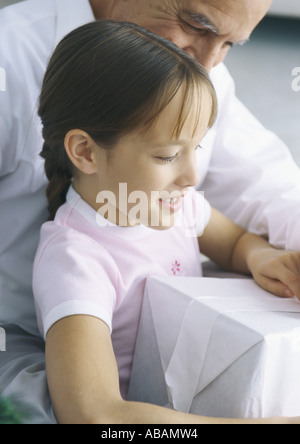 Girl holding présent pendant que grand-père regarde par-dessus son épaule Banque D'Images