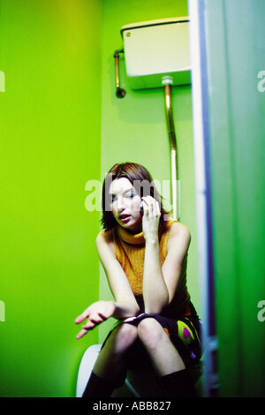 Femme assise sur les toilettes avec téléphone portable Banque D'Images