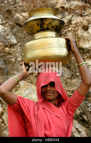 Smiling woman vêtue de rose sari est de transporter l'eau sur la tête des pots de Rajasthan Inde Banque D'Images