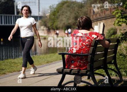 Camden, Londres du Nord : une femme solitaire lit un livre le long du Grand Union Canal près de Camden, Londres du Nord - bateaux sur le canal en arrière-plan Banque D'Images
