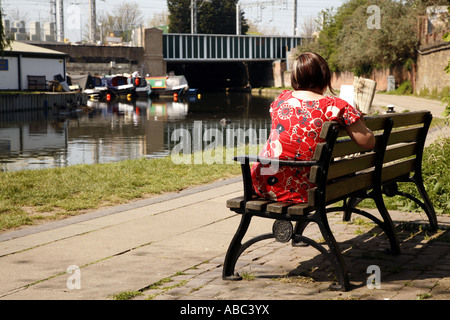 Camden, Londres du Nord : une femme solitaire lit un livre le long du Grand Union Canal près de Camden, Londres du Nord - bateaux sur le canal en arrière-plan Banque D'Images