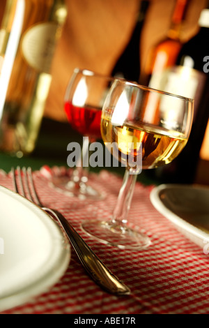 Deux verres de vins blanc et rouge avec des plaques et tapis de table à carreaux sur fourche quatre bouteilles de vin sur l'arrière-plan Banque D'Images