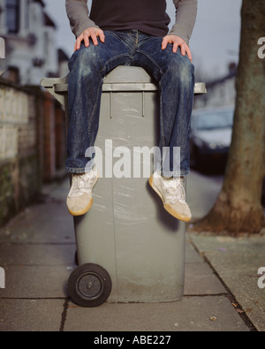 Un jeune homme assis sur un wheelie bin Banque D'Images