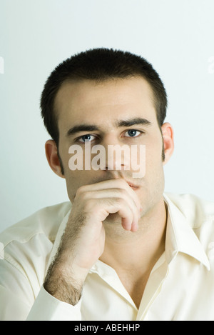 Man looking at camera, main devant la bouche, tête et épaules, portrait Banque D'Images