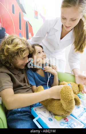 Garçon et fille jouant médecin, infirmière à la recherche sur leurs épaules Banque D'Images