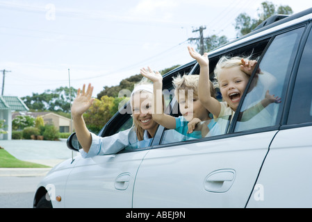 La mère et deux enfants agitant des vitres de voiture, looking at camera Banque D'Images
