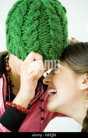 Deux jeunes femmes avec des chefs d'amis ensemble, l'un tirant Knit hat au-dessus des yeux tandis que l'autre rit Banque D'Images