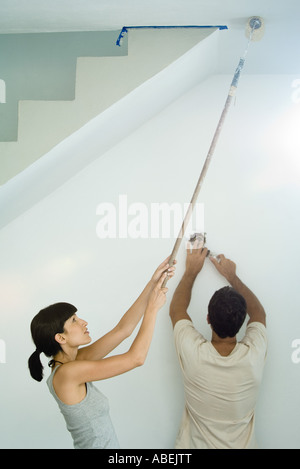 Plafond peinture femme avec rouleau à peindre tandis que l'homme change lightbulb Banque D'Images