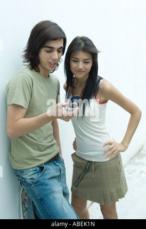 Jeune couple leaning against wall, looking at cell phone Banque D'Images