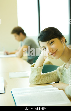 Female college student sitting at table with book, smiling at camera Banque D'Images