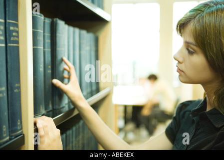 Female college student taking book from shelf in library Banque D'Images